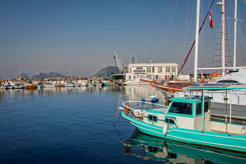 A scooter crosses the end of the street, the turquoise boat sits in the marina, and a couple walk down towards the water. (2 of 3)