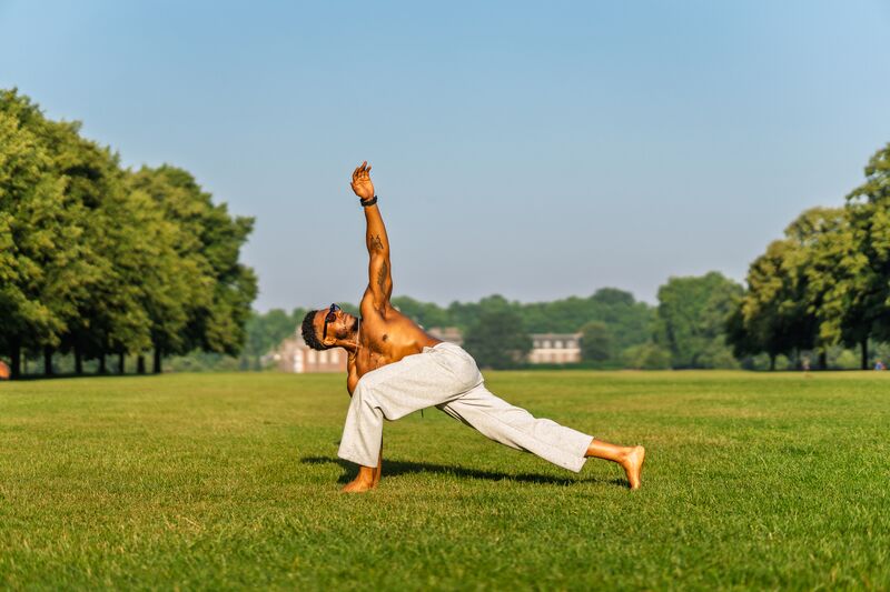 Joshua Silvera, sports therapist, stretching barefoot on grass in a London park